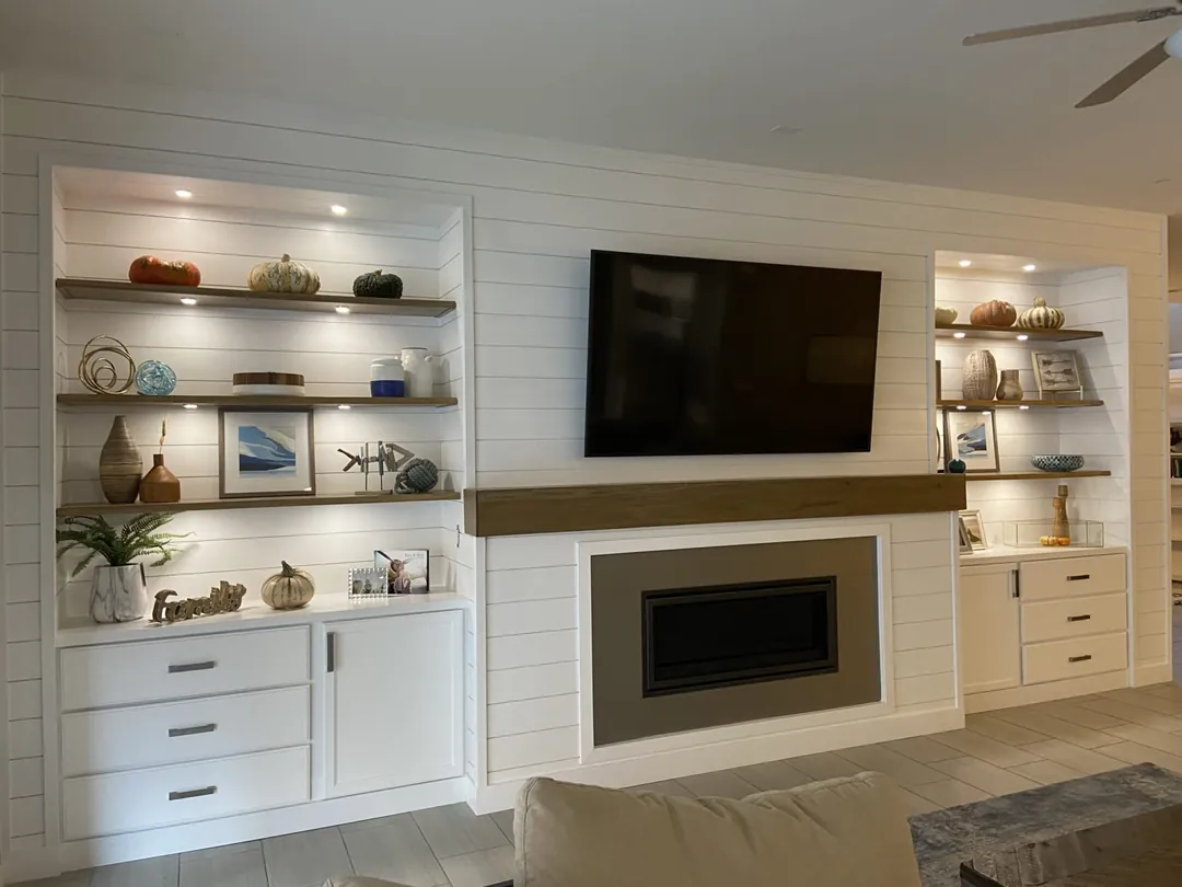 White shiplap fireplace wall with a wood box mantel, TV and lit open shelves
