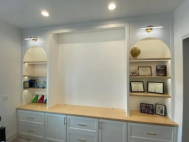 Office wall of white cabinets with arched lit niches and a clear maple desktop
