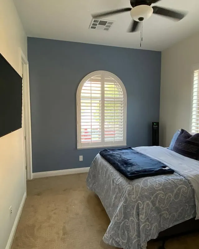 Guest room with a blue accent wall behind the bed and an arched window