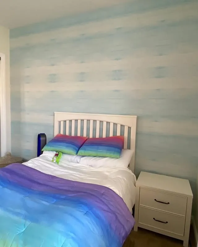 Child's bedroom with a soft blue striped wallpaper wall