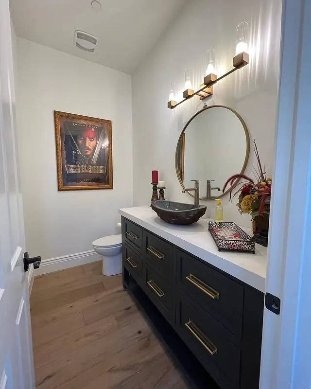 Powder room with a dark vanity and a round brass mirror