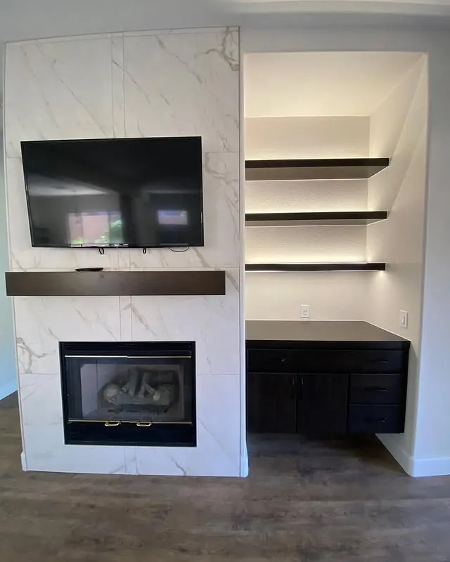 Fireplace clad in white Calacatta-look porcelain beside a floating dark media cabinet and shelves