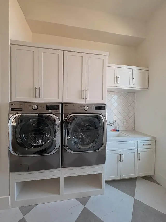 Front-loading washer and dryer raised on white cabinetry with cubbies below
