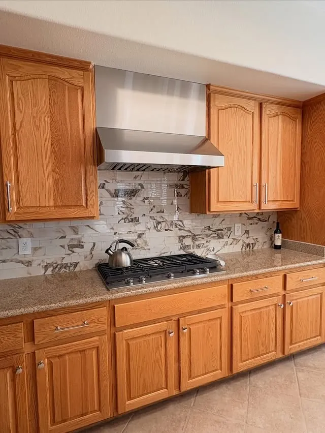 Stainless range hood with a wood surround running up to the ceiling between oak cabinets