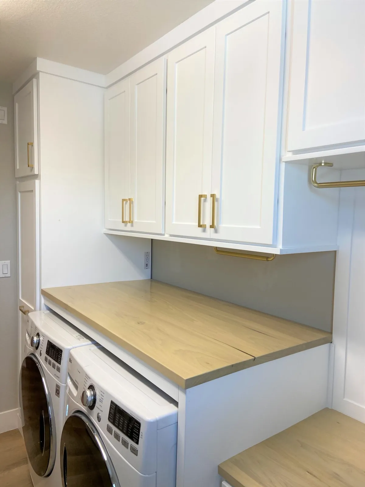 White laundry cabinets with brass pulls over a front-loading washer and dryer