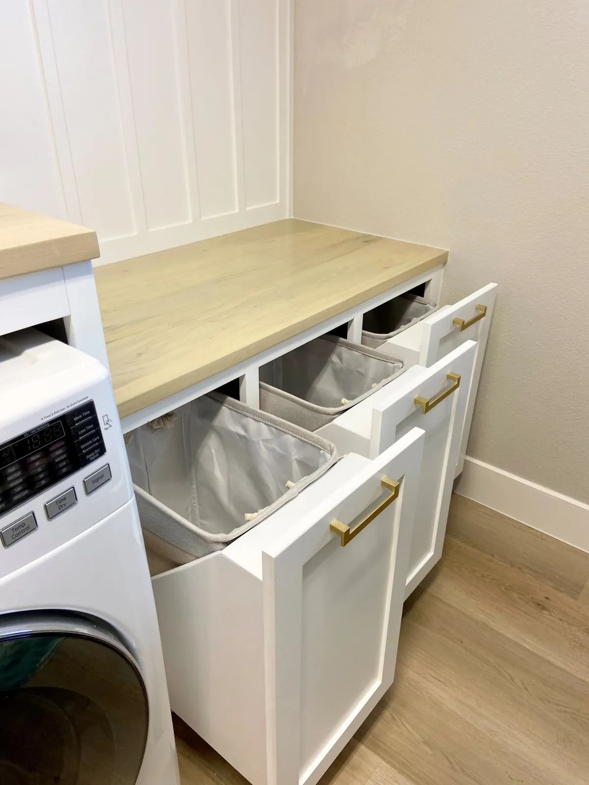 Two tilt-out laundry hampers pulled open under a white-washed wood counter
