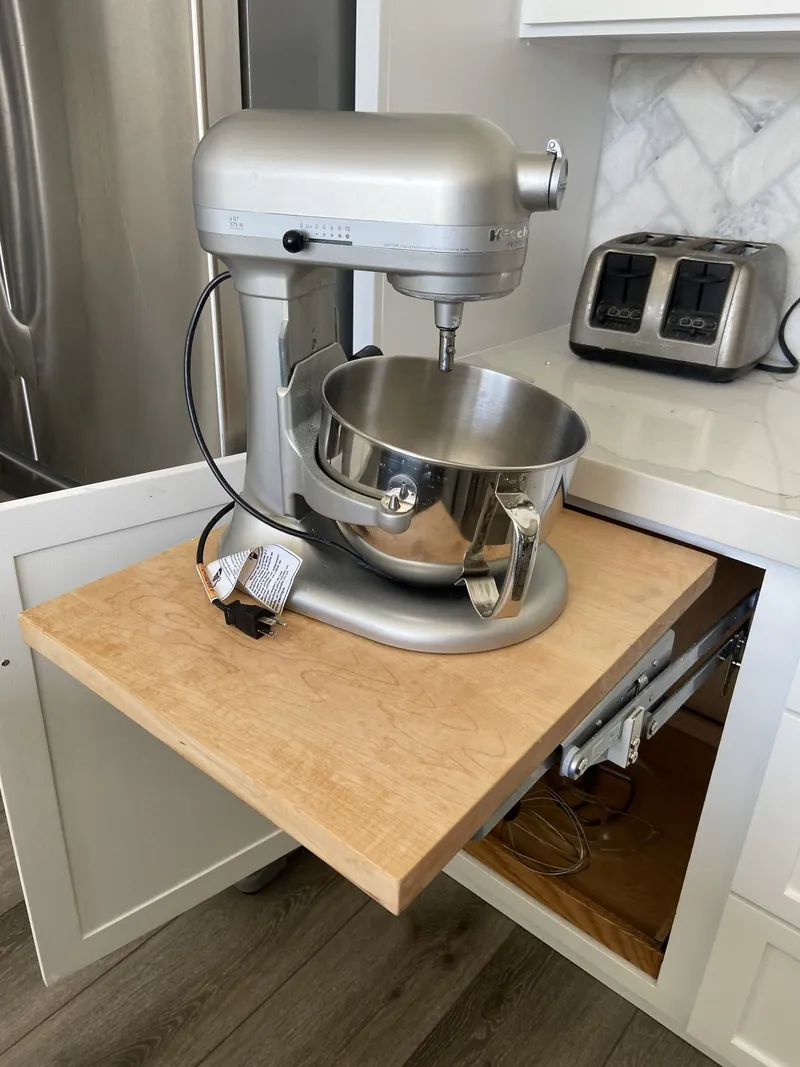 A stand mixer on a lift shelf rising out of a white base cabinet