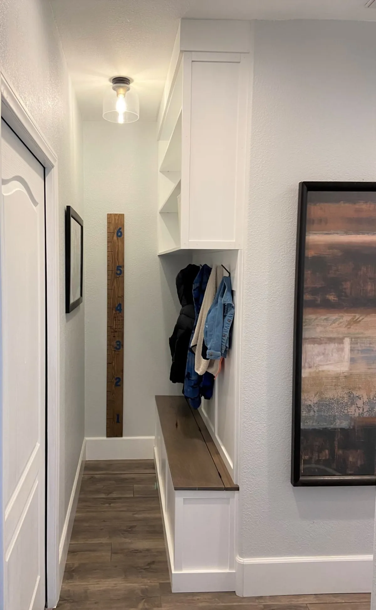 Narrow mudroom with a wood bench, coat hooks and a tall cabinet