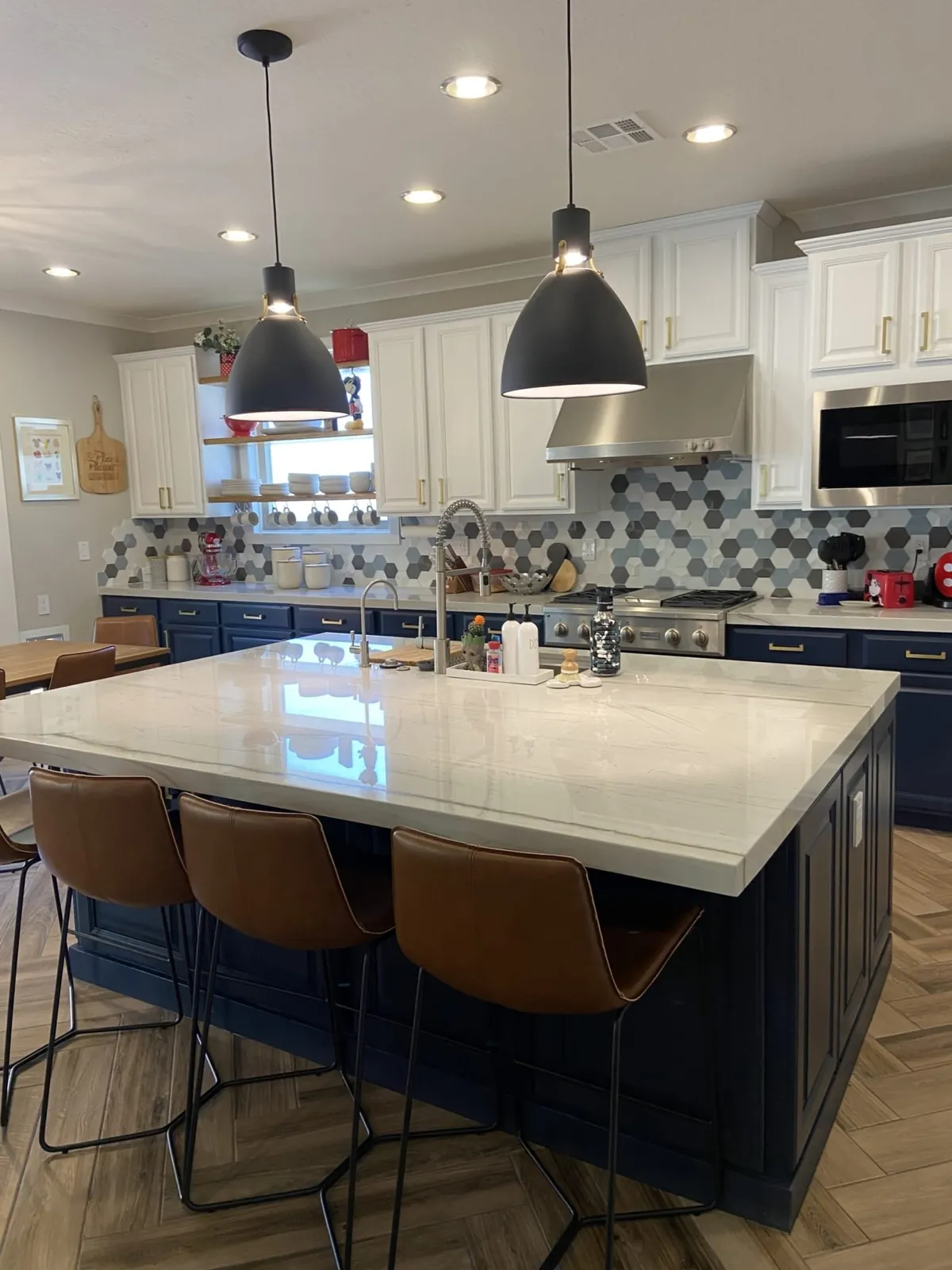 White kitchen with a navy island, brass pendants and a marble-look counter