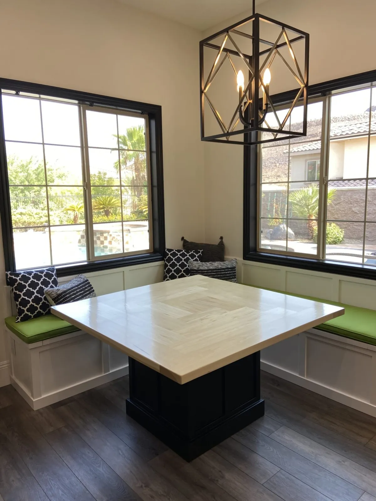Finished breakfast nook: white banquette with green cushions, square table and a cage pendant