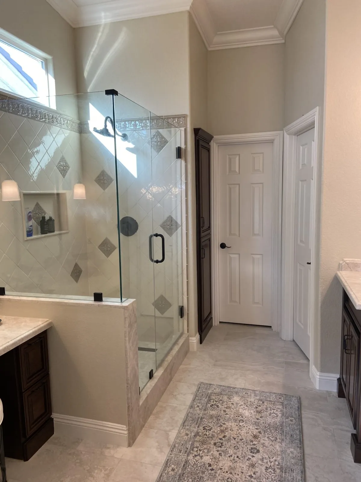 Primary bathroom with a glass shower, dark wood vanity and patterned rug